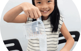 A student pouring water into a a long plastic beaker to measure volume